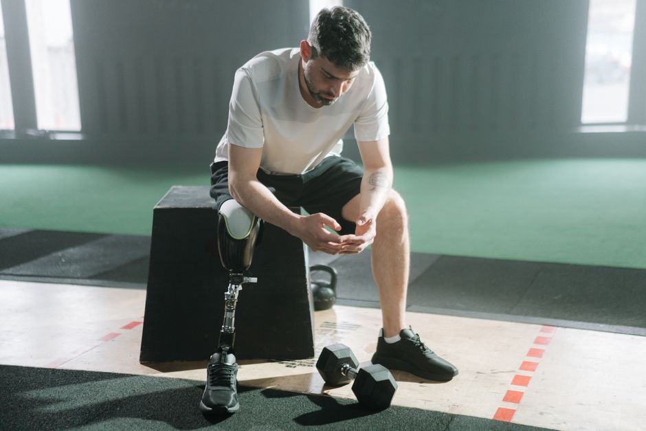Homem com prótese de perna descansando após treino de musculação em academia moderna.