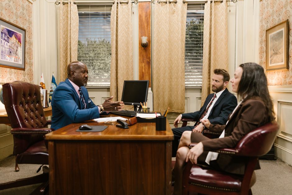 Três pessoas participando de uma reunião de negócios em um ambiente formal, com foco na colaboração e negociação empresarial.