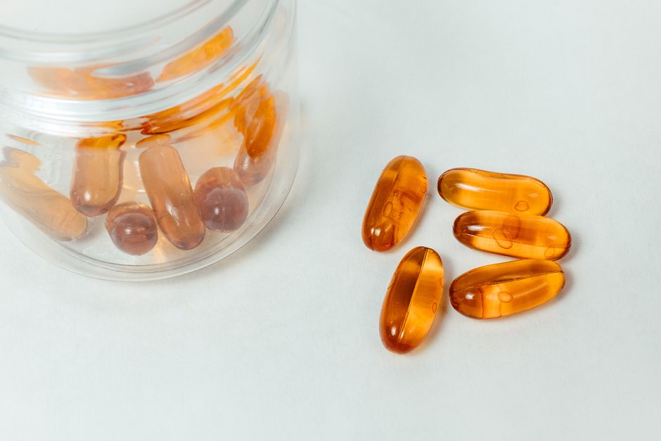 Imagem de cápsulas de óleo de peixe, com algumas dentro de um pote de vidro e outras espalhadas ao lado, destacando um suplemento vitamínico.
