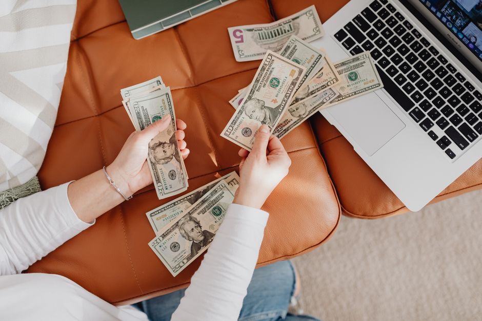Pessoa organizando dinheiro em uma mesa de trabalho ao lado de um laptop, representando gestão financeira ou planejamento de orçamento.