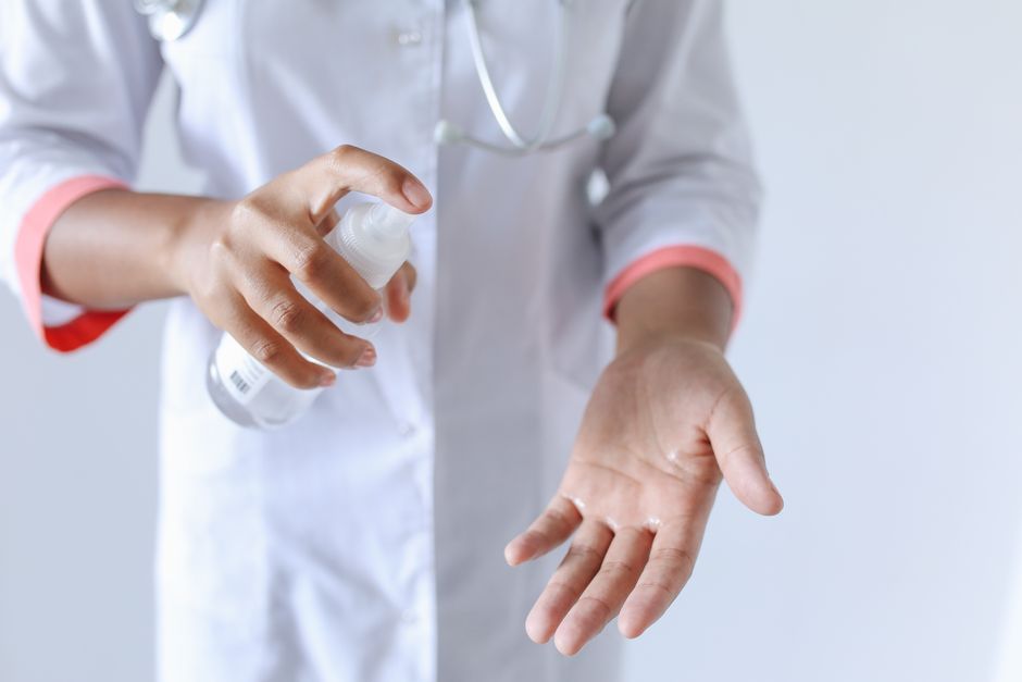 Imagem de uma profissional de saúde sanitizando as mãos com álcool gel, destacando práticas de higiene e cuidado médico.