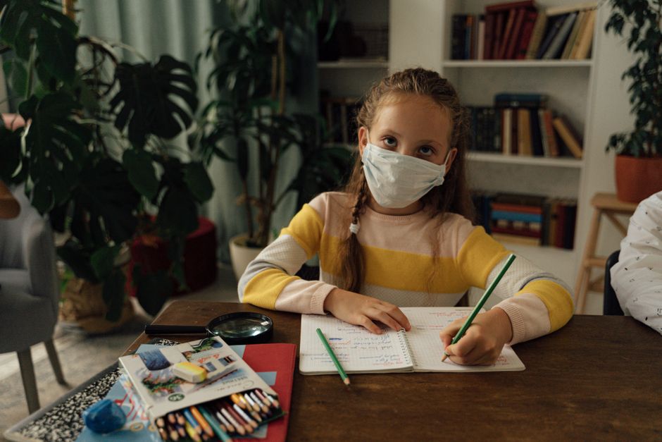 Menina estudando com máscara facial em um ambiente de leitura ou estudo, destacando cuidados durante a pandemia.