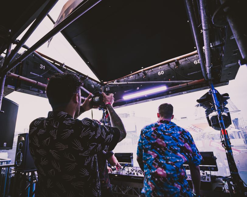 DJ tocando em um evento ao ar livre, com iluminação e equipamento de som destacado em um ambiente urbano moderno.