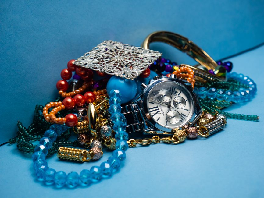 Coleção de joias e acessórios em uma superfície com fundo azul, destacando o contraste entre objetos elegantes e as cores vibrantes.