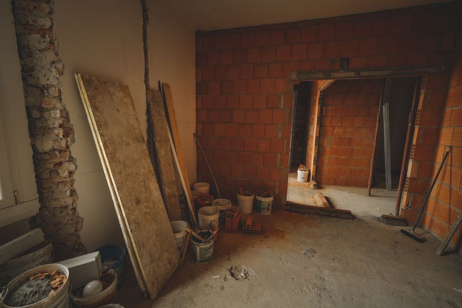 Imagem de um ambiente em reforma, com paredes de tijolos expostos e materiais de construção empilhados, simbolizando o processo de renovação e construção de espaços internos.