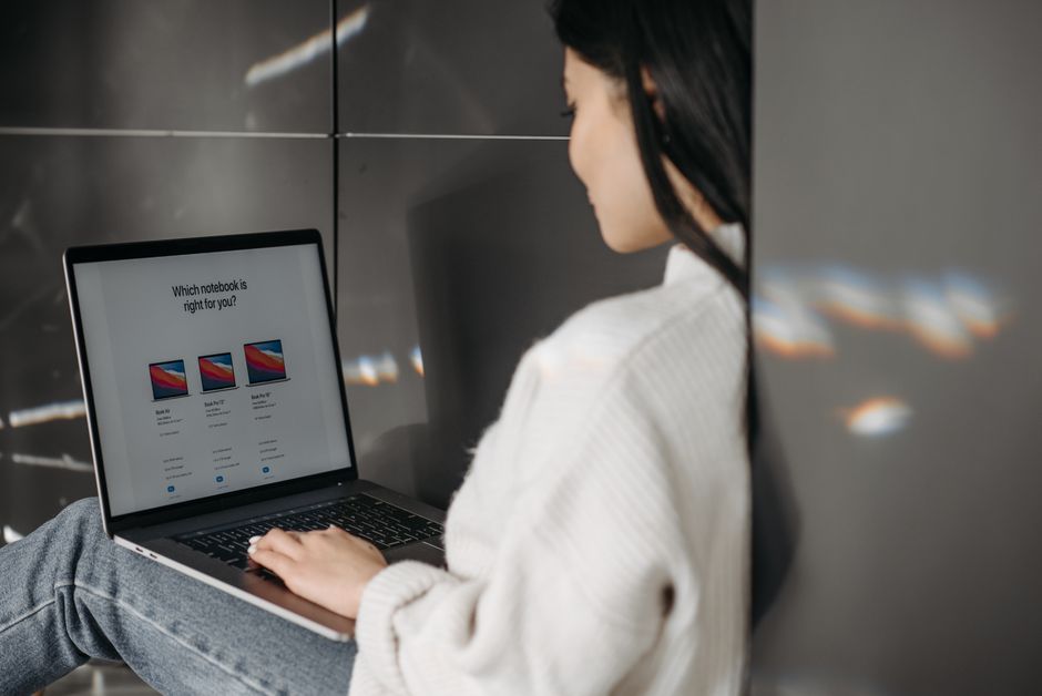 Mulher avaliando opções de notebooks em um ambiente moderno, representando escolhas de tecnologia para trabalho ou estudo.
