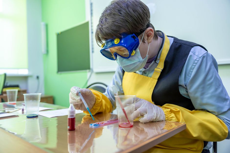 Jovem cientista realizando experimentos em um laboratório, com equipamentos de proteção e materiais científicos sobre a mesa.