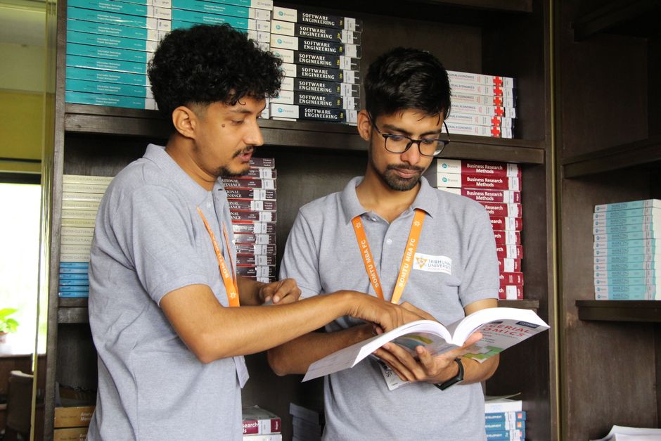Dois estudantes analisando um livro em uma biblioteca ou livraria, com estantes de livros ao fundo, focados no tema de estudos acadêmicos ou pesquisa.