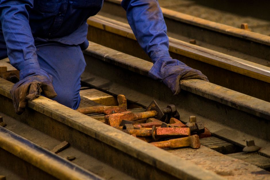 Funcionário realizando manutenção ou inspeção em trilhos de trem em ambiente industrial ou ferroviário.