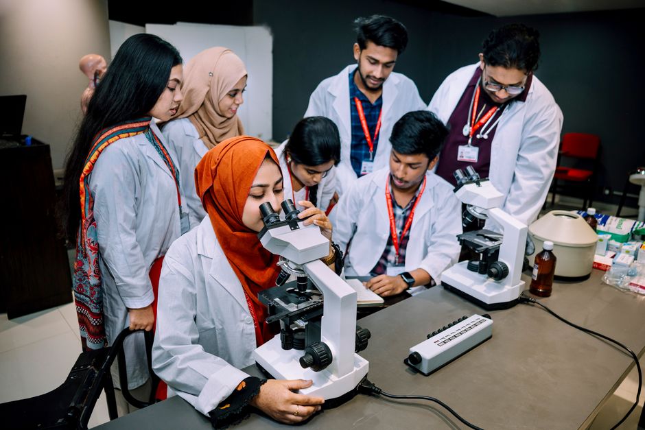 Grupo de estudantes e profissionais de ciências da saúde realizando análise de amostras usando microscópios em laboratório.