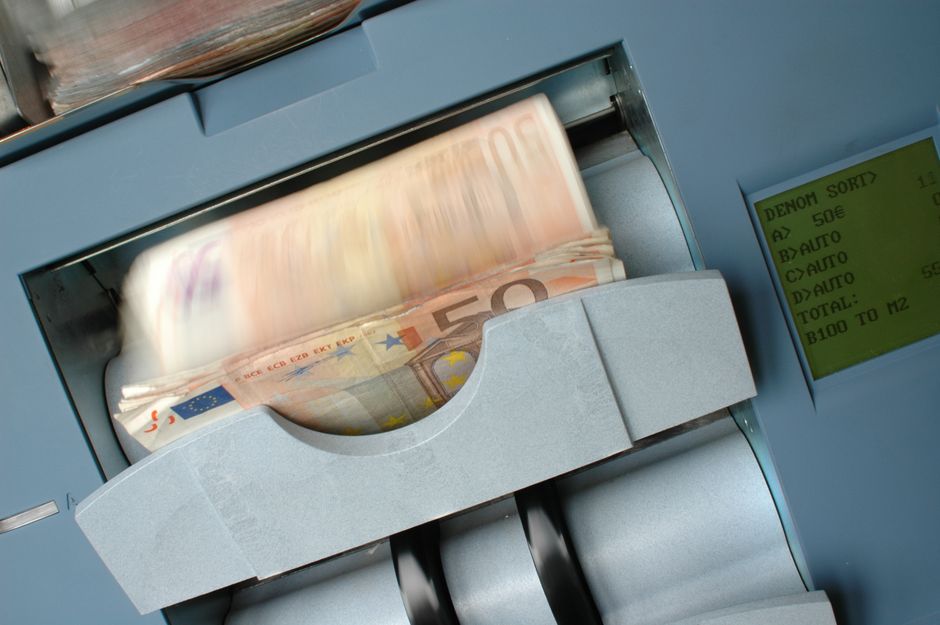 Imagem de uma máquina de contar dinheiro automática inserindo cédulas de euro, representando temas de transações financeiras e automação bancária.