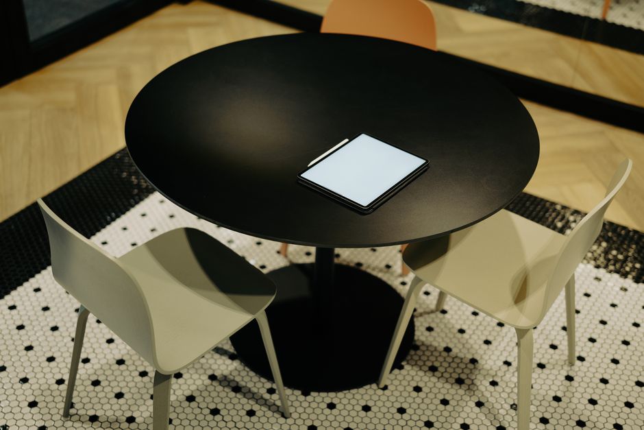 Imagem de uma mesa de reunião com um tablet no centro, sugerindo um ambiente de trabalho ou discussão de ideias em um espaço moderno.