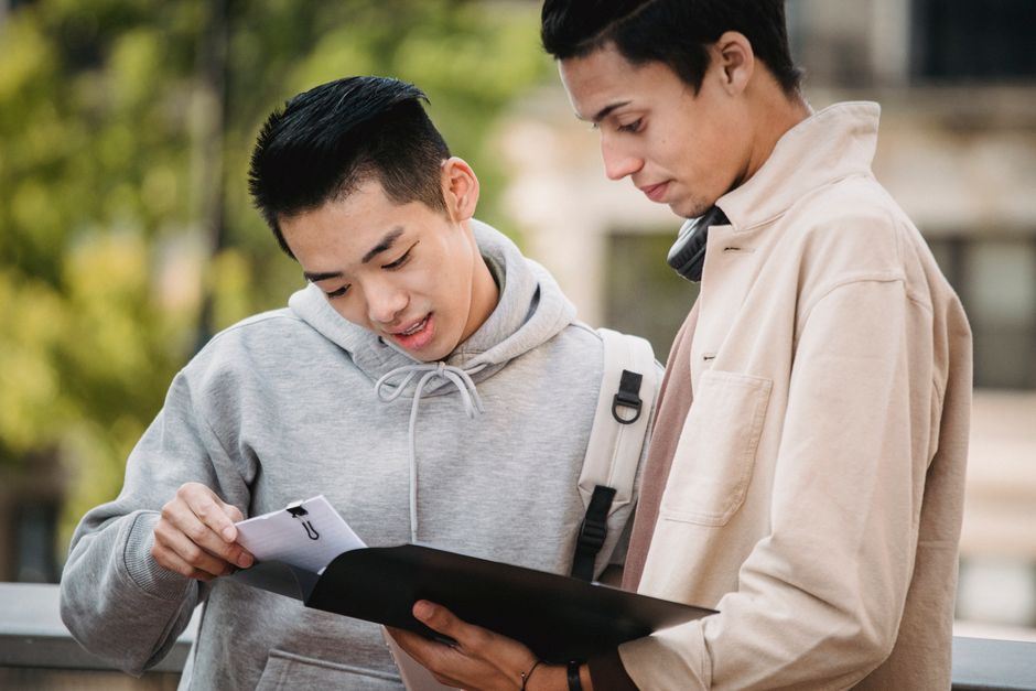 Dois jovens estudantes conversando ao ar livre, discutindo conteúdo acadêmico, em um ambiente de estudo ao ar livre