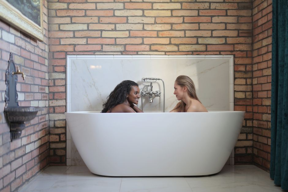 Duas mulheres se apoiando uma na outra dentro de uma banheira, simbolizando conexão e bem-estar entre amigas ou parceiras.
