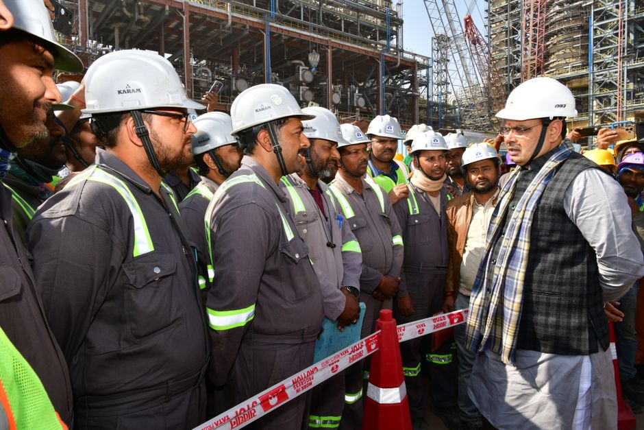 Grupo de trabalhadores da construção civil participando de uma reunião ou inspeção na obra com um engenheiro ou gestor responsável.
