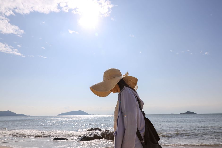 Pessoa caminhando na praia sob um céu ensolarado, transmitindo sensação de calma e conexão com a natureza.