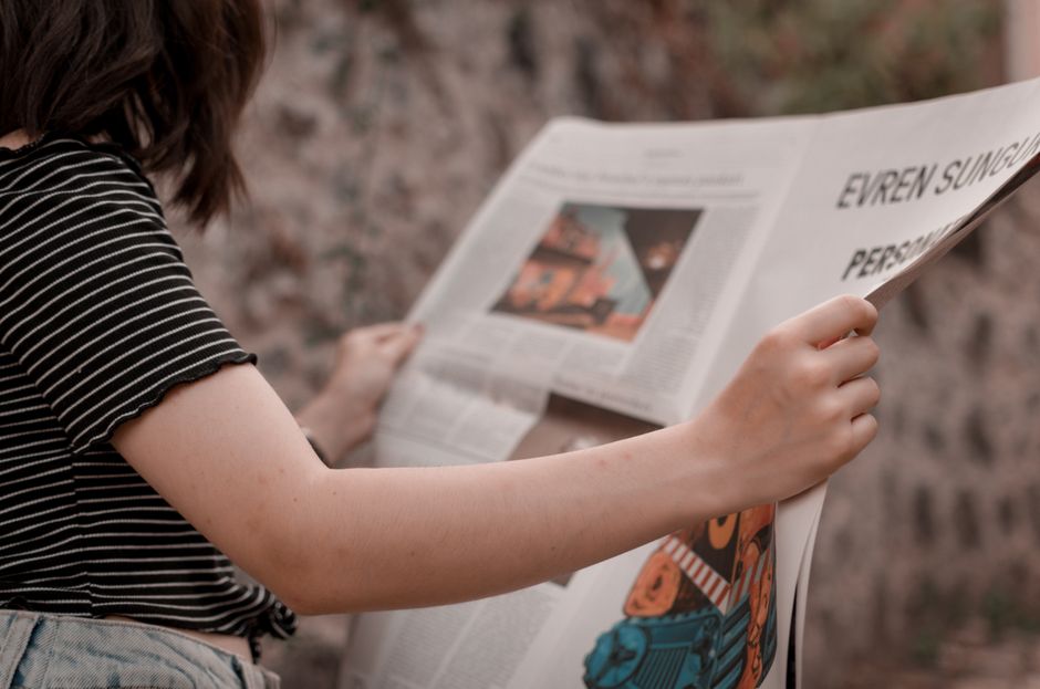 Pessoa lendo um jornal ao ar livre, representando consumo de notícias e informação atualizada.