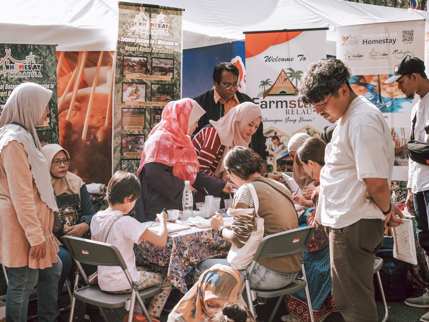 Grupo de pessoas participando de uma feira ou evento cultural, interagindo com atividades e exposições ao ar livre.