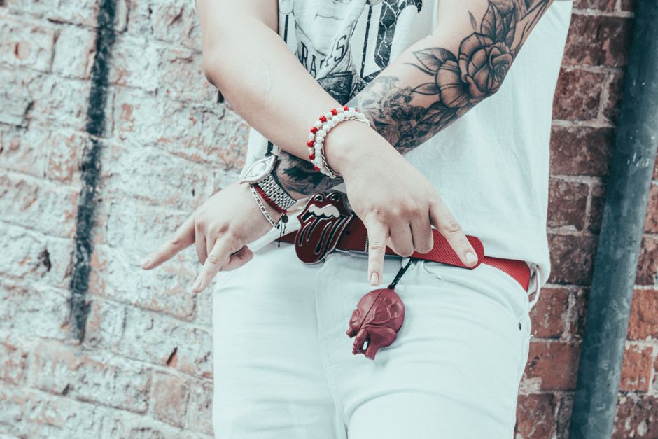 Pessoa exibindo acessórios e tatuagens com uma parede de tijolos ao fundo, refletindo estilo alternativo e personalidade expressiva.