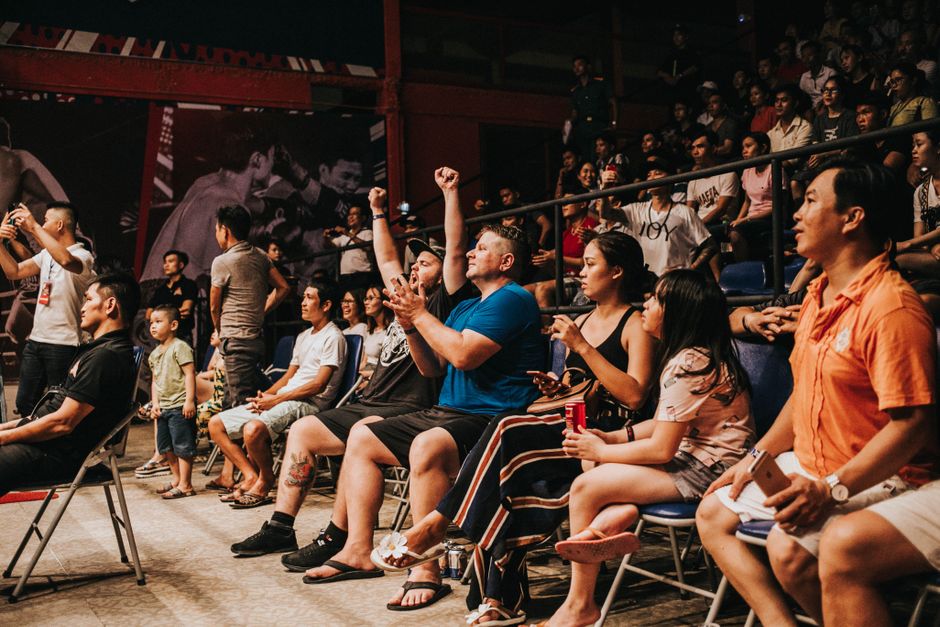 Pessoas assistindo a um evento ao vivo com reações de entusiasmo e envolvimento.
