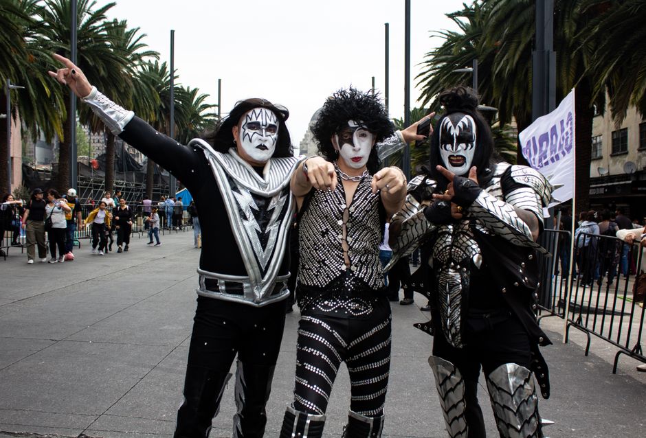 Grupo de pessoas fantasiadas representando os integrantes da banda de rock Kiss em uma celebração pública ao ar livre.
