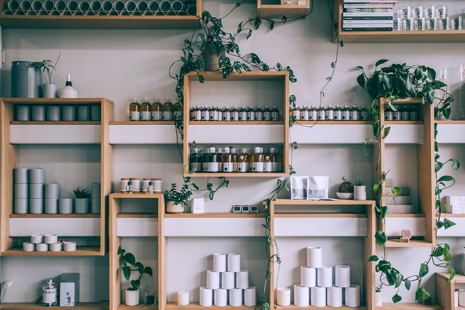Imagem de uma parede com prateleiras de madeira exibindo frascos de produtos naturais e plantas, criando um ambiente acolhedor e sustentável