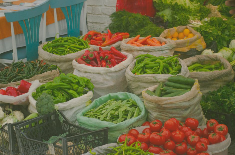 Imagem de uma feira de hortaliças com sacos repletos de pimentões, tomates, cenouras, e outros vegetais frescos, ideal para ilustrar temas sobre alimentação saudável e agricultura sustentável.