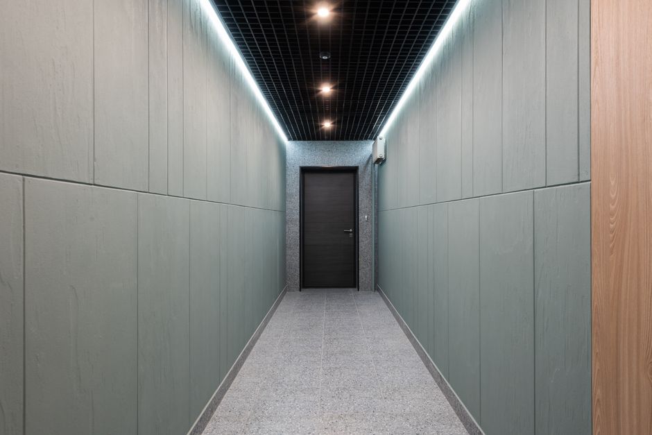 Corridor moderno e minimalista em ambiente empresarial, com iluminação indireta e porta de entrada ao fundo.