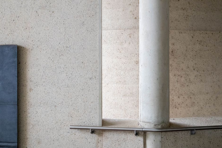 Imagem de uma parede com textura de concreto e uma coluna de suporte, destacando o ambiente de construção ou espaço arquitetônico moderno.