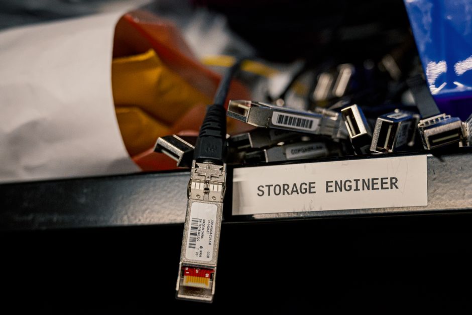 Imagem que representa o tema de armazenamento de dados e tecnologia, com cabos de rede e dispositivos de armazenamento numa área de trabalho profissional.