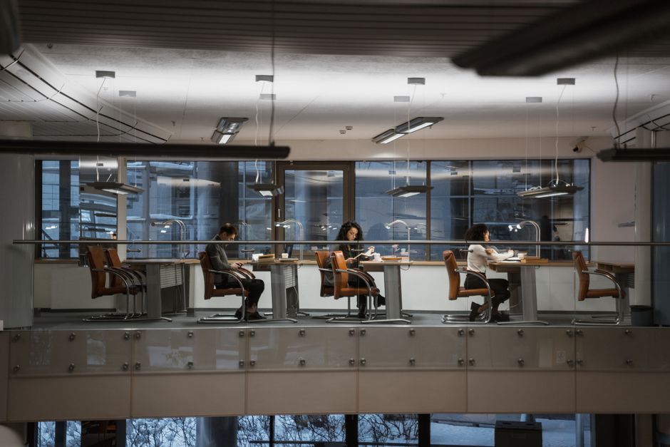 Pessoas trabalhando individualmente em um ambiente de escritório moderno com amplas janelas e iluminação adequada ao final do dia, focando no tema de produtividade e trabalho remoto.