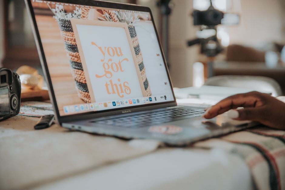Pessoa trabalhando em um laptop com uma mensagem motivacional na tela, em um ambiente de trabalho informal ou home office.