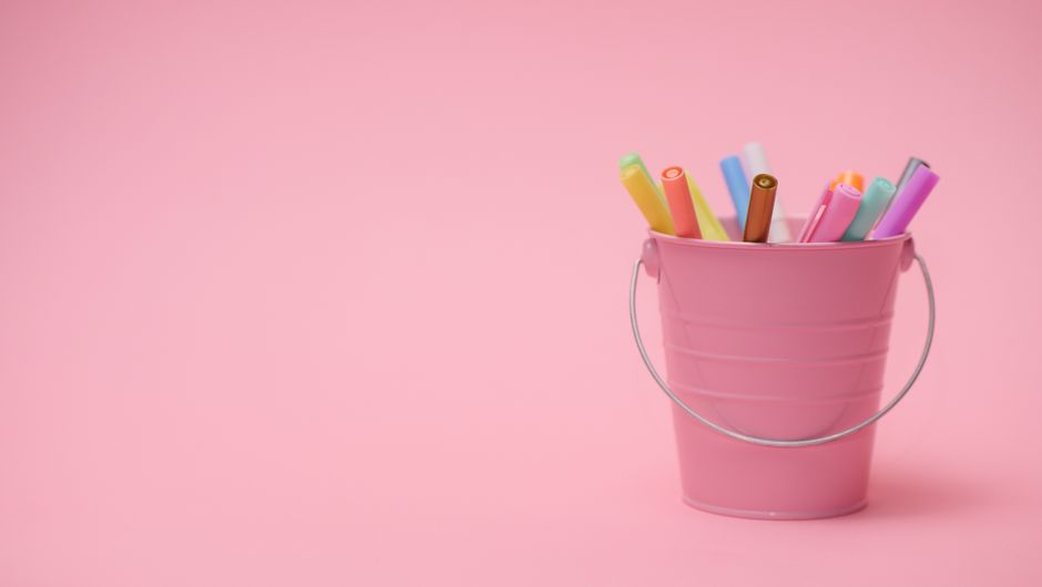 Imagem de um balde rosa com canetas coloridas, simbolizando organização e criatividade em um ambiente de trabalho ou estudo.