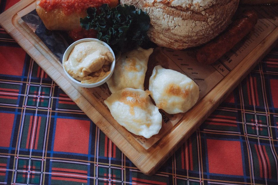 Prato de comida típica com pães, queijo, salsicha e molho, em ambiente que remete à culinária tradicional brasileira ou inglesa.