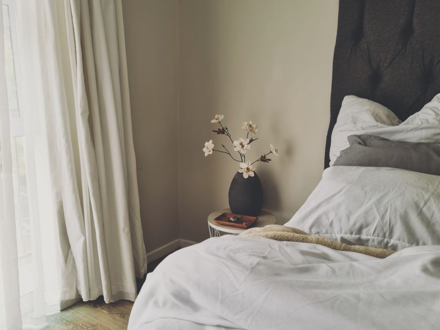 Cama em um quarto com decoração minimalista e vaso de flores na mesinha ao lado, transmitindo aconchego e paz para um ambiente doméstico.