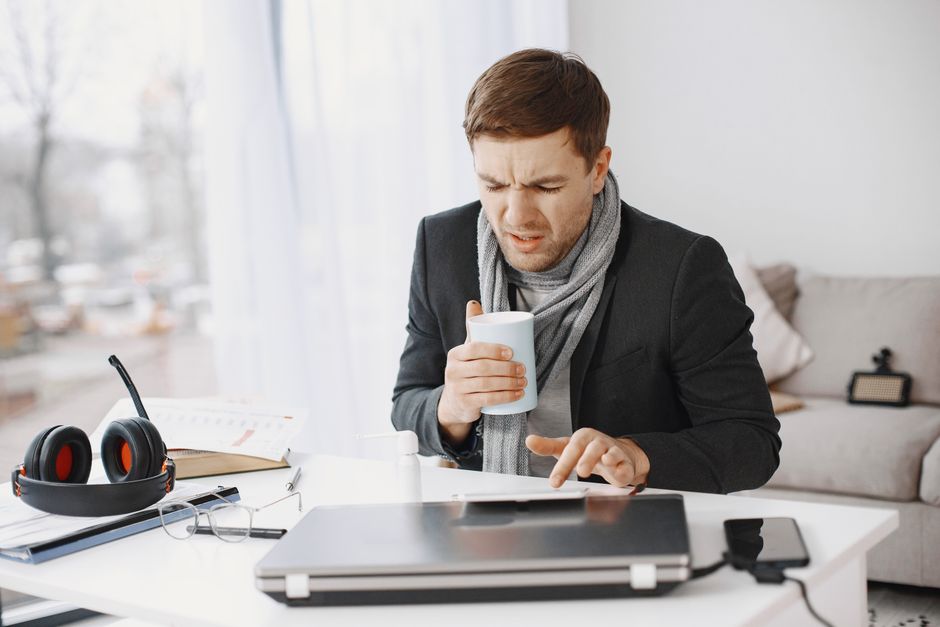 Homem irritado segurando uma xícara de café na frente do computador, simbolizando frustração ou cansaço no ambiente de trabalho remoto.