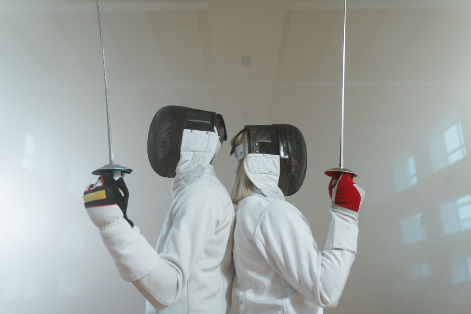 Dupla de profissionais realizando uma atividade de esportes radicais em uma parede de vidro, utilizando equipamentos de proteção e roupas específicas.