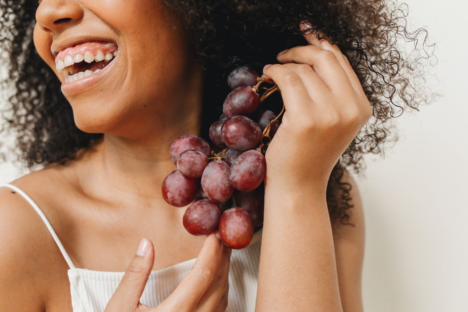Mulher sorridente segurando um cacho de uvas, transmitindo alegria e bem-estar.
