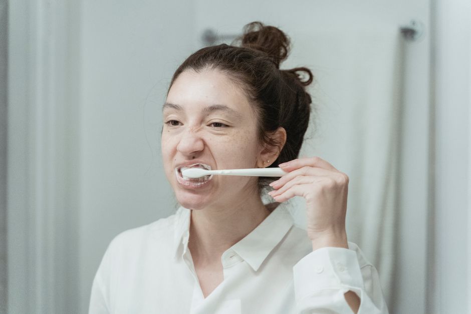 Mulher escovando os dentes enquanto se prepara para o dia, em um ambiente de banheiro ou quarto
