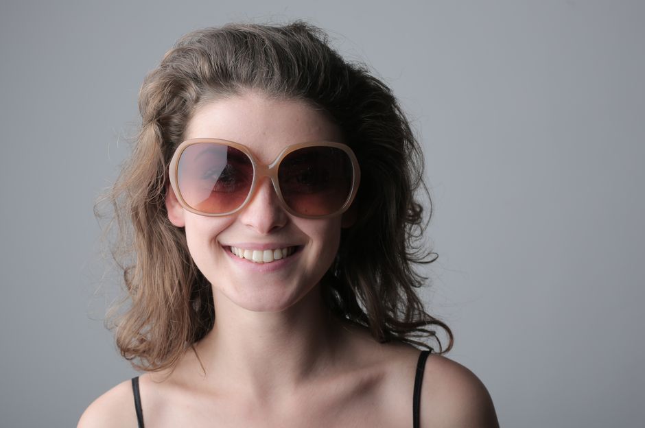 Mulher sorridente usando óculos grandes e escuros, simbolizando diversão e estilo em um ambiente descontraído.