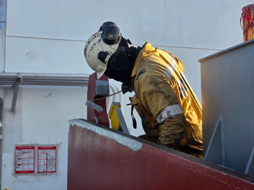 Profissional de segurança realizando inspeção ou manutenção em ambiente industrial externo, usando equipamento de proteção completo.