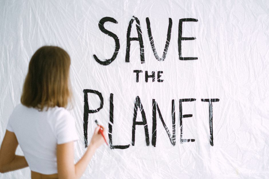 Pessoa escrevendo na parede a frase 'Save the Planet', promovendo consciência ambiental.