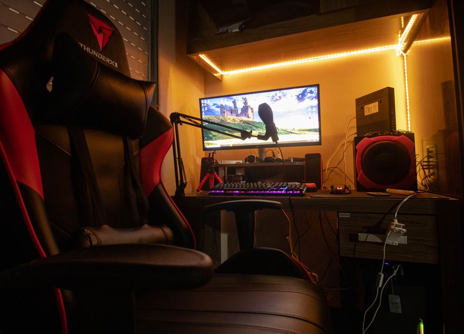 Estação de trabalho de gamers ou criadores de conteúdo com foco em tecnologia e entretenimento, destacando um computador com periféricos e iluminação ambiente acolhedora.