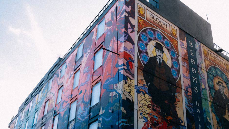 Mural artístico em um edifício de cidade que destaca a cultura e a arte urbana, combinando elementos gráficos vibrantes e uma figura central estilizada.