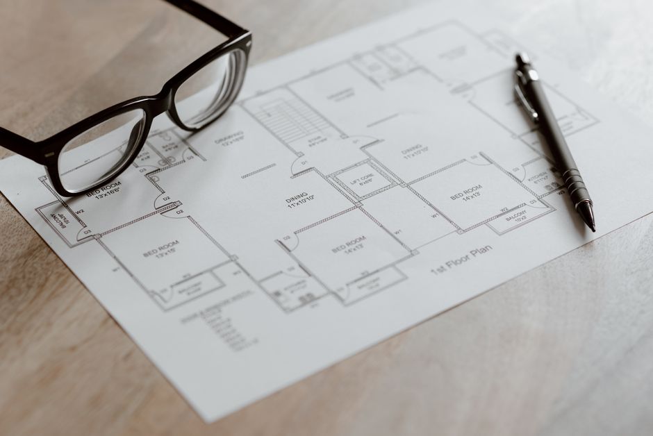 Imagem de um projeto de arquitetura de uma casa, com óculos e uma caneta sobre o papel, ideal para um artigo sobre planejamento de construção ou design de interiores.