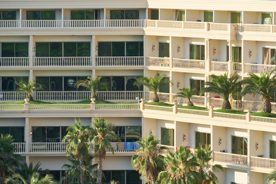 Fachada de um edifício residencial alto com varandas decoradas com palmeiras, transmitindo uma atmosfera de conforto e tranquilidade em um ambiente de luxo e lazer.