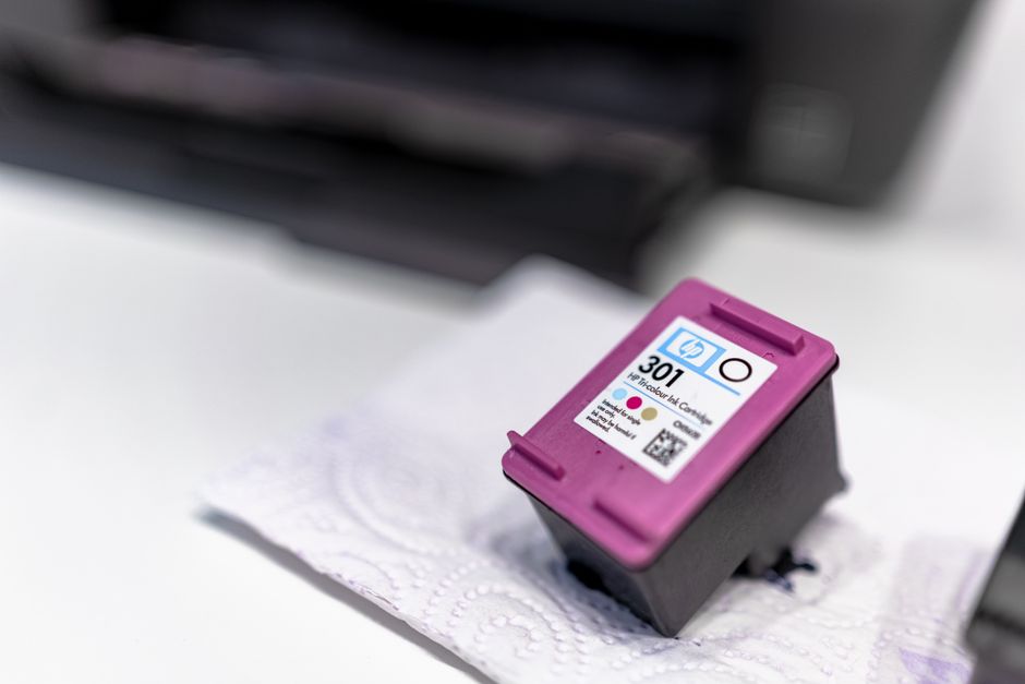 Tampa de tinta de impressora colorida sobre papel toalha, representando manutenção ou abastecimento de equipamentos de impressão.