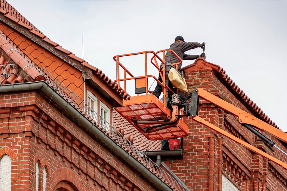 Profissional realizando manutenção em estrutura de edifício residencial com uso de torre de elevação.