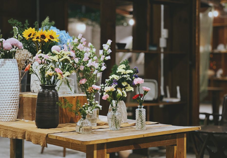 Imagem de uma mesa decorada com diversos vasos de flores coloridas, ideal para ilustração de temas sobre decoração, arranjos florais ou eventos ao ar livre.