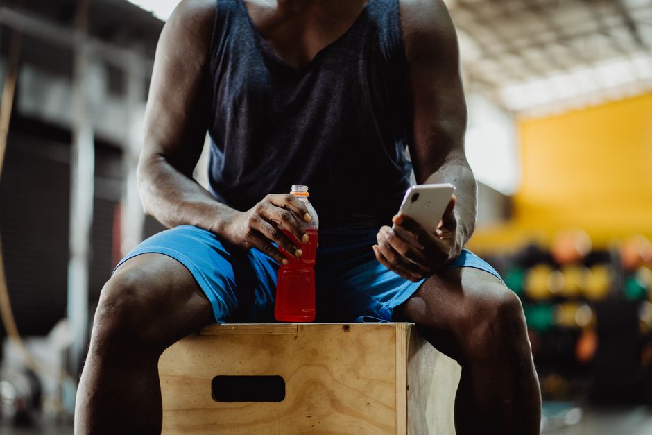 Atleta em treino relaxando enquanto verifica o celular após o exercício na academia.